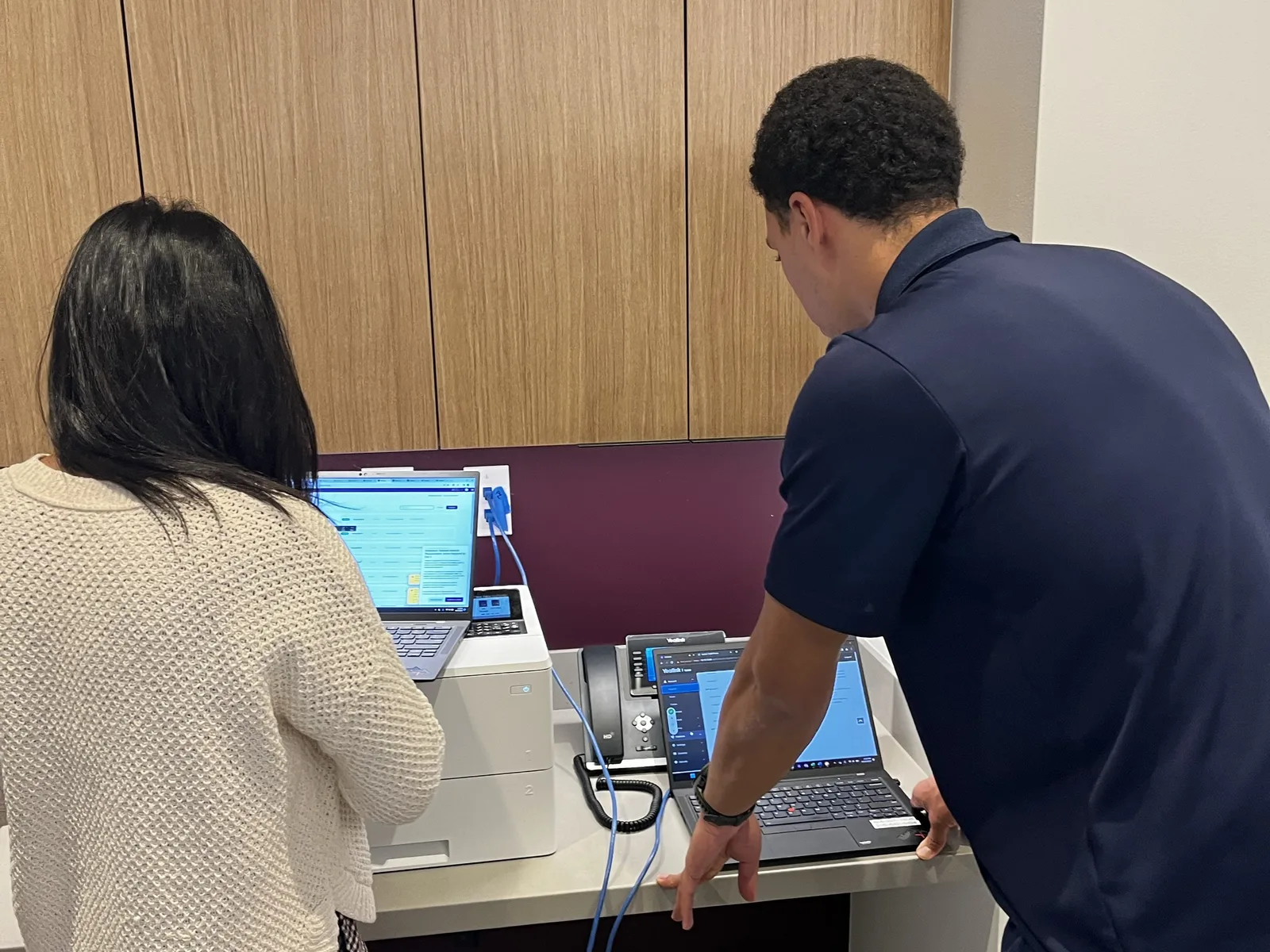 A Methodology IT engineer working at a laptop beside a client staff member at their front desk